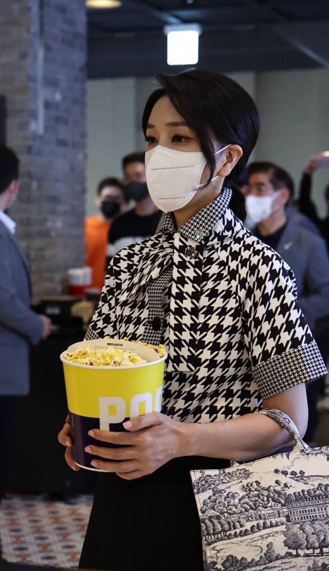2022년 6월, 영화관람 일정 중의 김건희 여사. 하운드투스 프린트의 반팔 셔츠는 디올 제품으로 약 700만원 대. 당시 국내 미출시 제품이었다. 가방은 디올의 ‘북토트’ 풍의 캔버스 백으로 20만원 대 국내 중소브랜드 제품이었다. 해당 제품은 즉시 완판되며 반짝 유